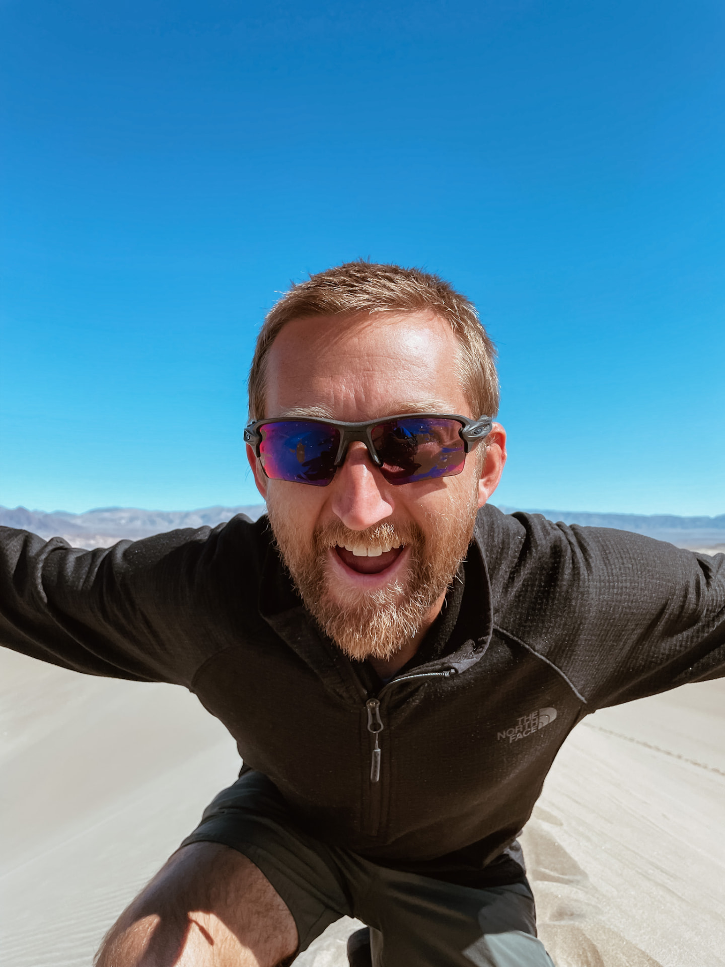 Coach Drew Ewing outdoors on a sand dune with arms outstretched
